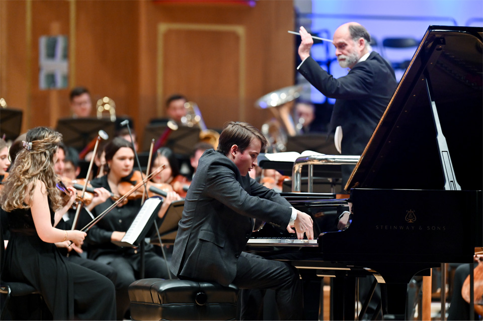 A male student passionately playing the piano, performing in an orchestra.